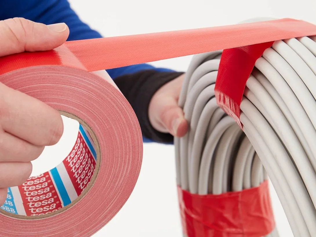 Opérateur industriel enroulant du ruban adhésif duct tape rouge Tesa 4688 autour de câbles pour les maintenir